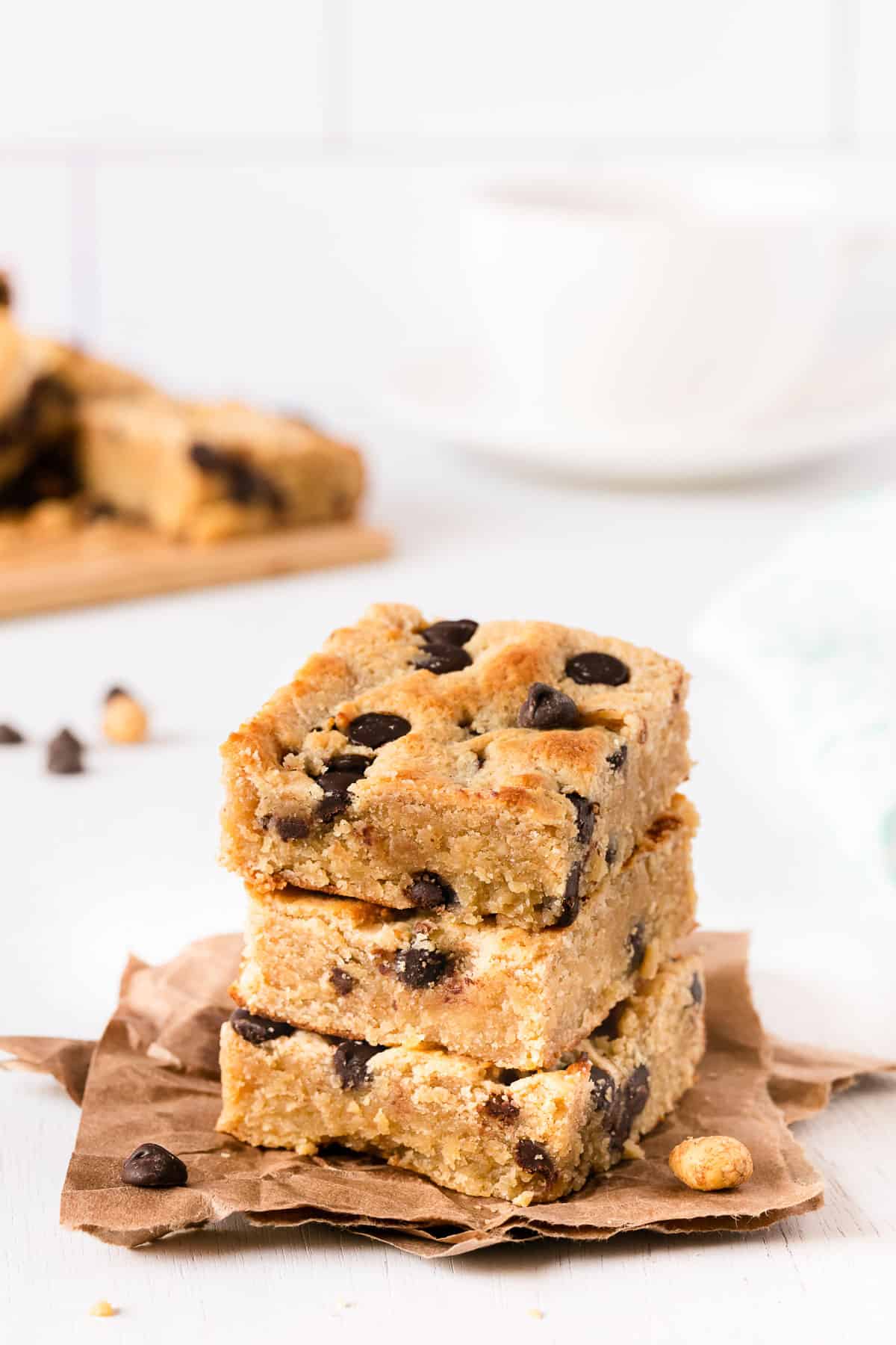 gluten free cookie bars stacked on top of each other on parchment paper, with a cup of coffee in the background