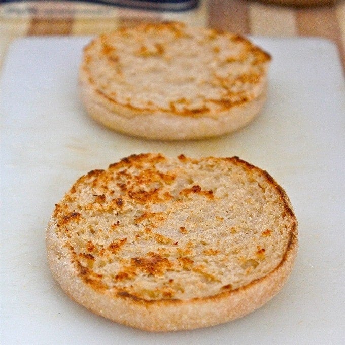 A low carb English muffin sliced in half, sitting on a white napkin on a wooden cutting board. Each half of the English muffin is perfectly toasted to golden brown.