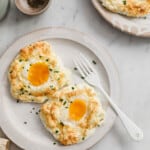 2 baked egg clouds, topped with chives, on a white ceramic plate with a fork