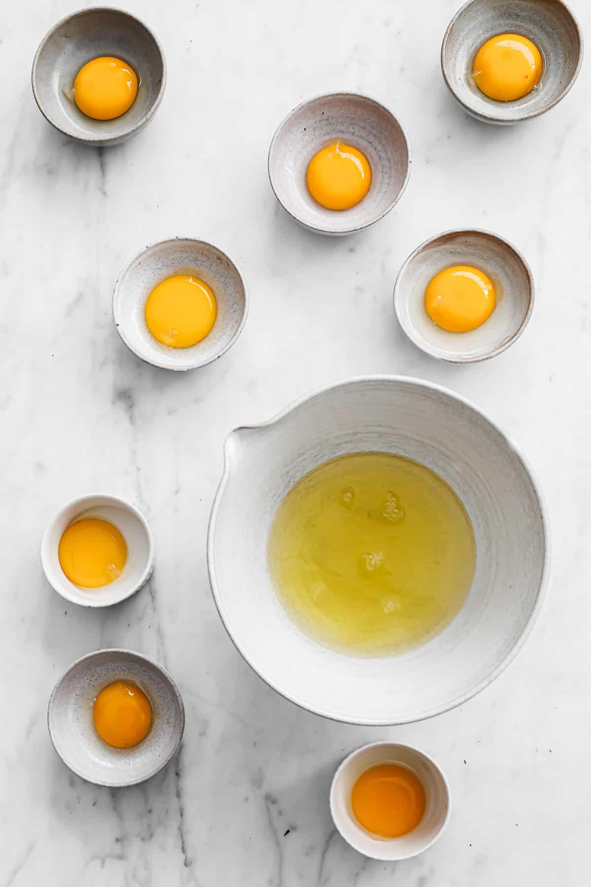 large ceramic bowl full of egg white, surrounded by ramekins with separated egg yolks