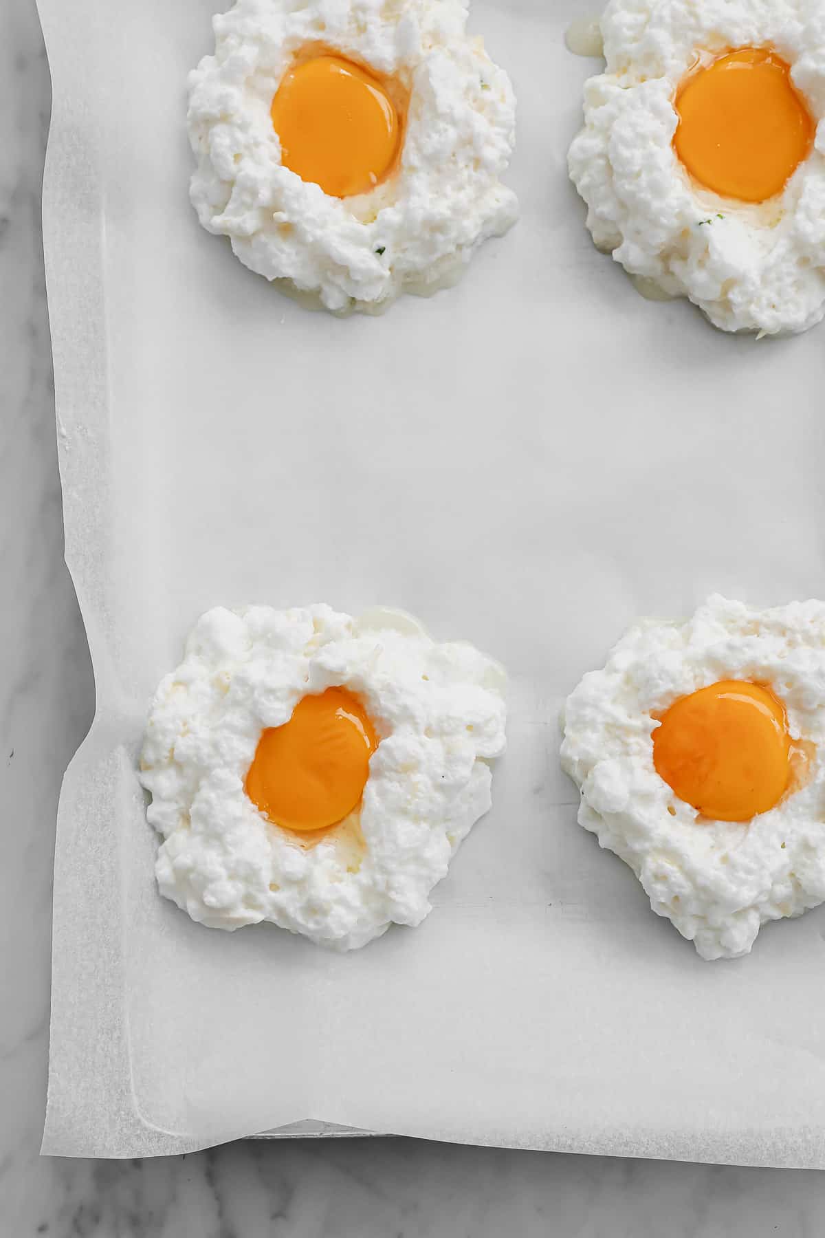 mounds of whipped egg whites, with a yolk placed in the center of each one, on a prepared baking sheet
