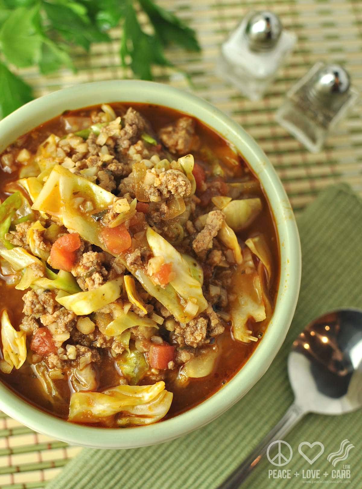 a bowl of cabbage roll soup, served with a spoon, salt, pepper, and garnished with parsley