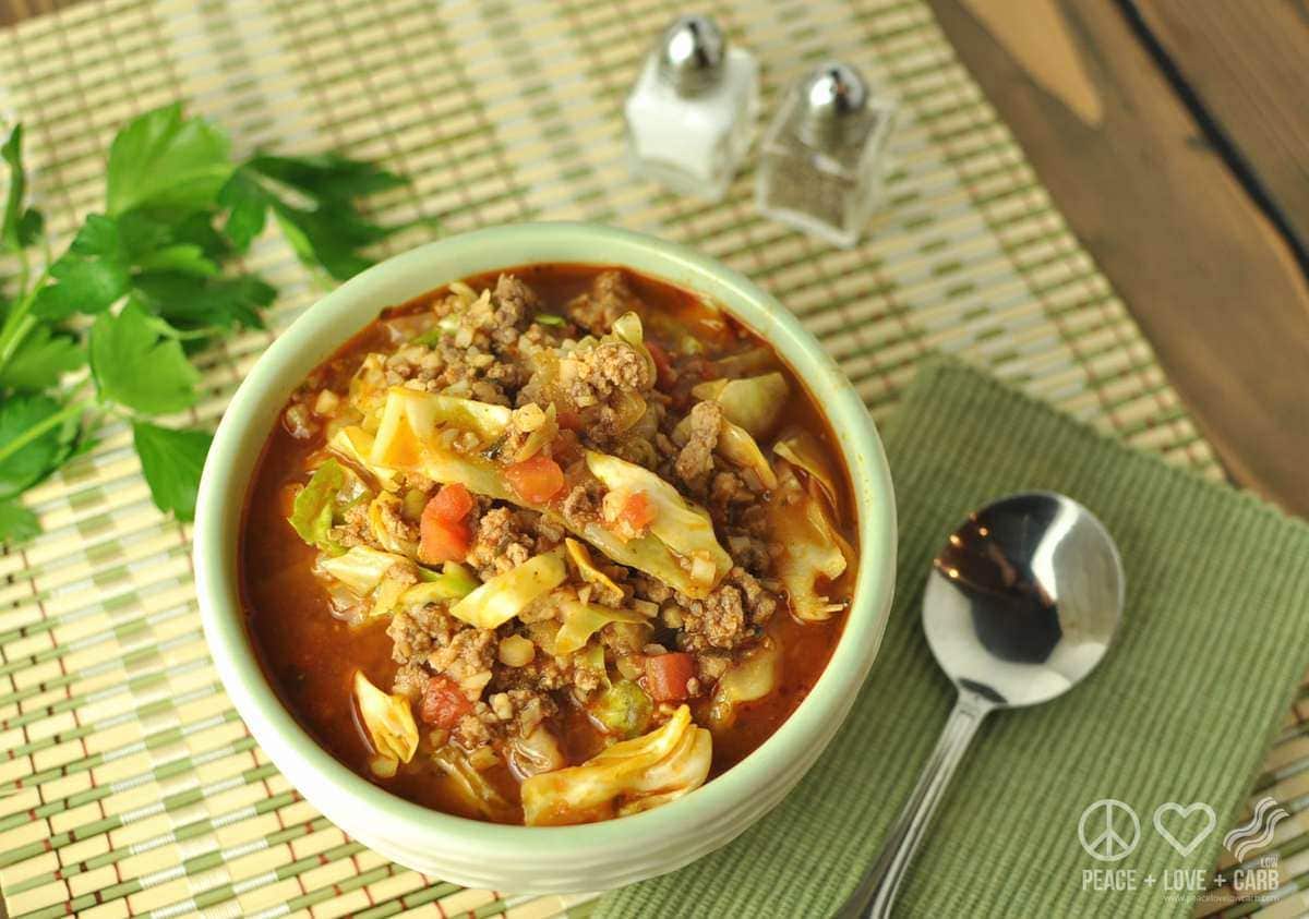 a bowl of cabbage roll soup, served with a spoon, salt, pepper, and garnished with parsley