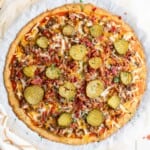 a keto bacon cheeseburger pizza with ground beef, bacon, cheese, pickles, onion and garlic