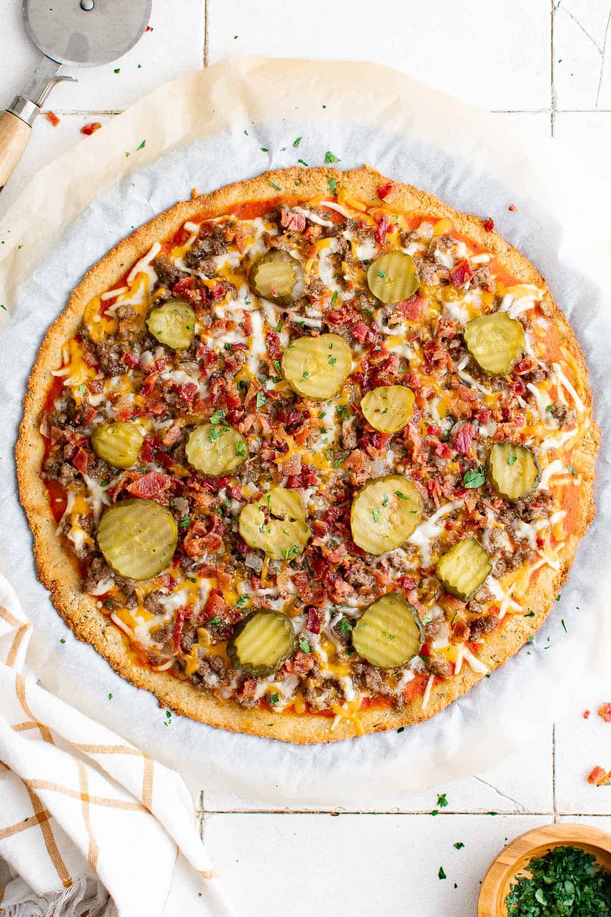 a keto bacon cheeseburger pizza with ground beef, bacon, cheese, pickles, onion and garlic