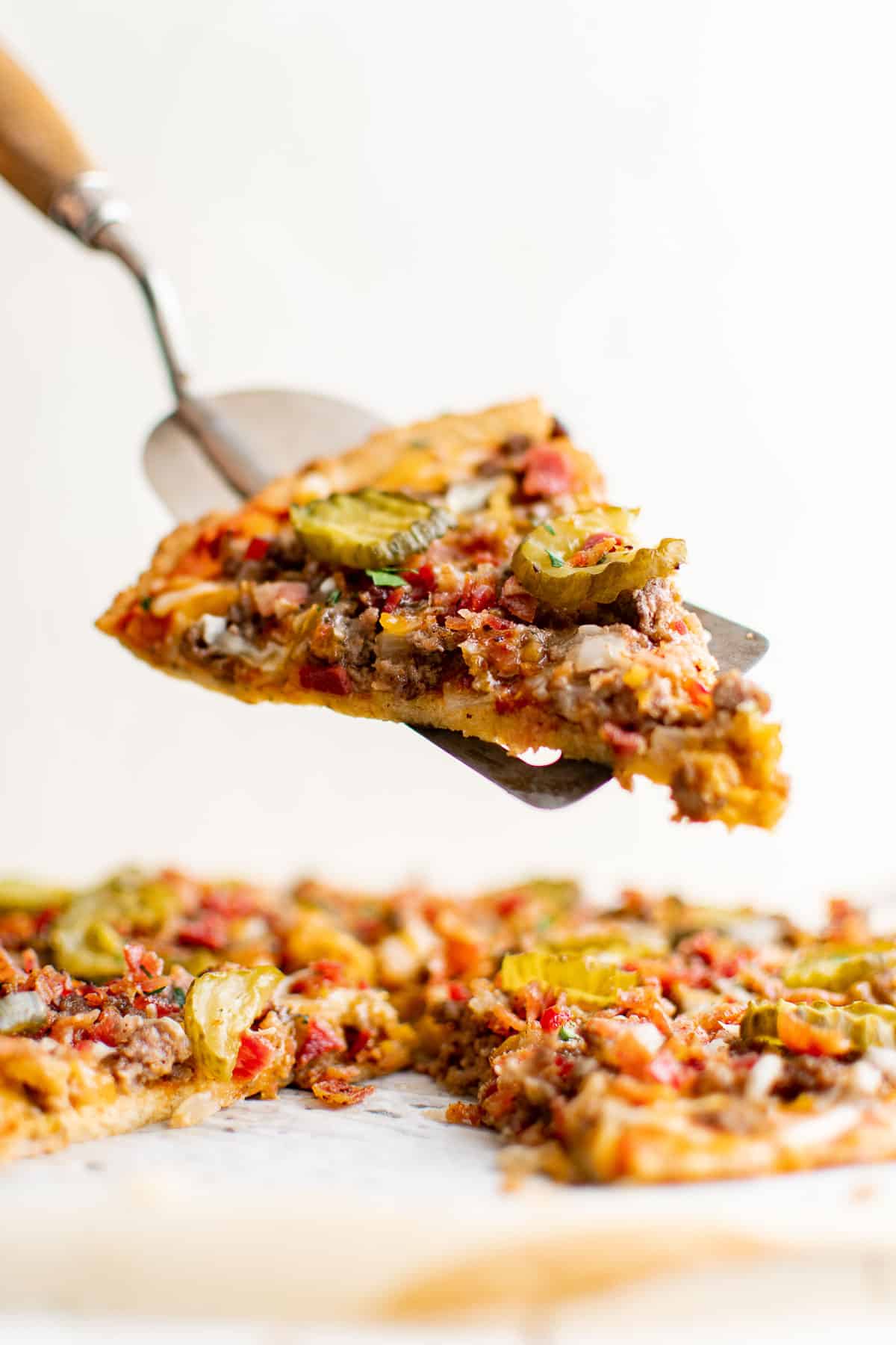cheeseburger pizza with ground beef, bacon, cheese, pickles, onion and garlic