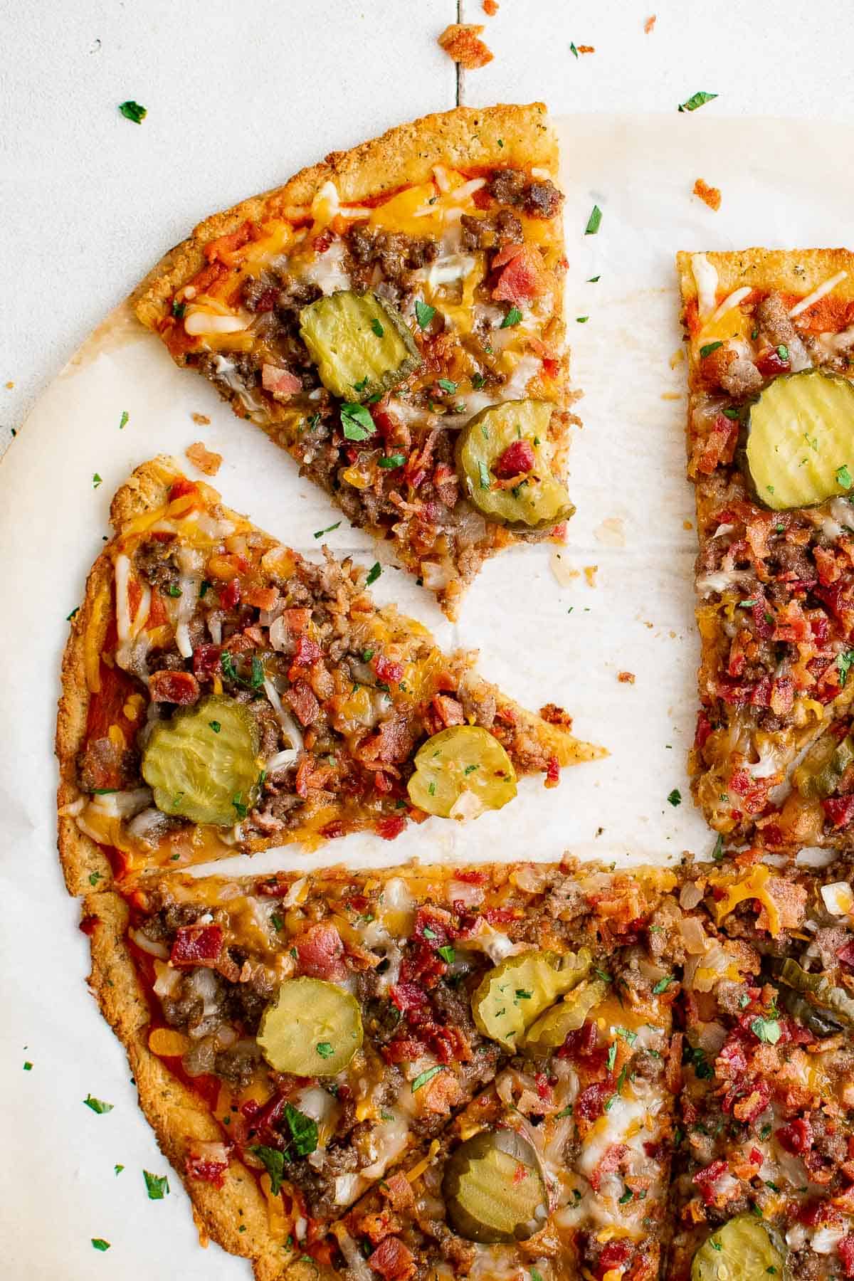 a keto bacon cheeseburger pizza with ground beef, bacon, cheese, pickles, onion and garlic