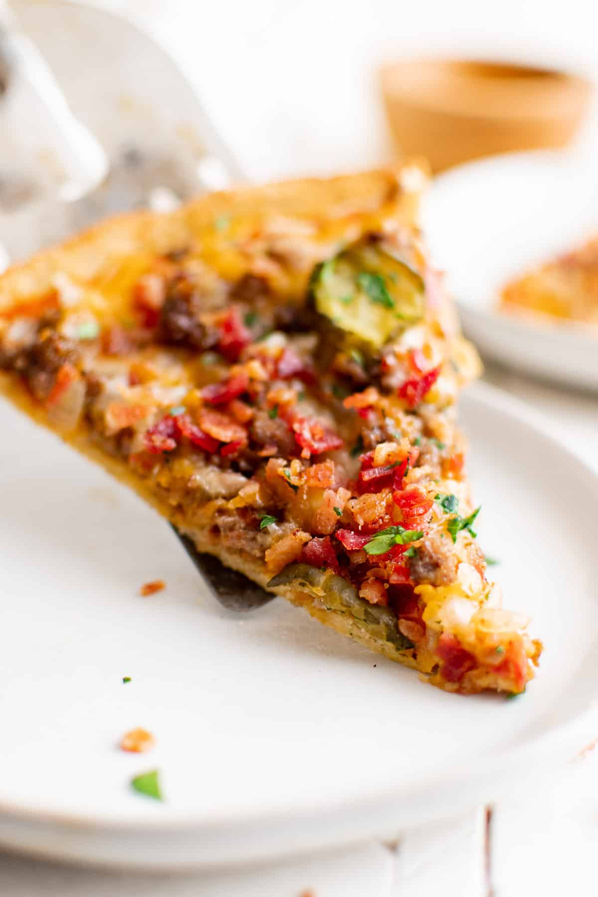 a slice of bacon cheeseburger pizza with ground beef, bacon, cheese, pickles, onion and garlic