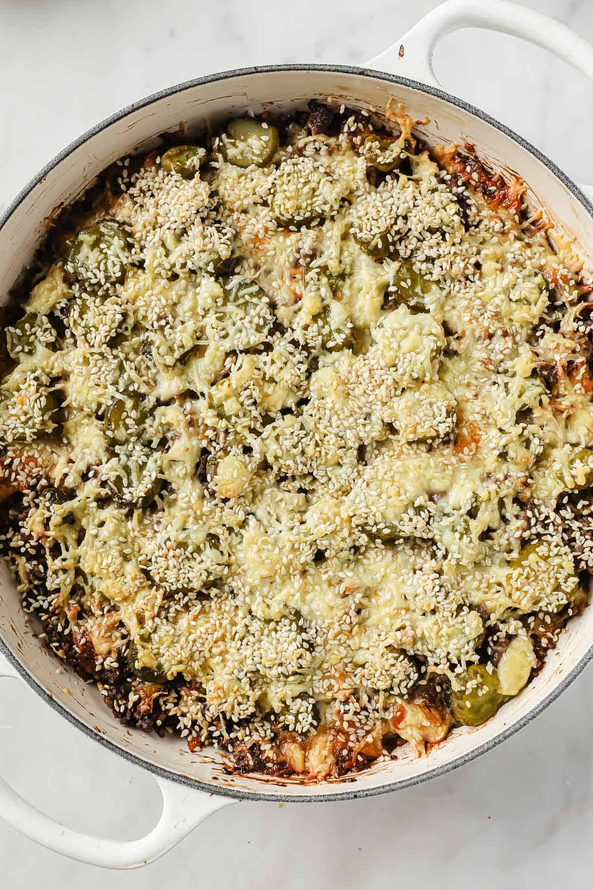 a cast iron pan, full of a casserole made with ground beef, burger sauce, cheese, pickles, onions and sesame seeds