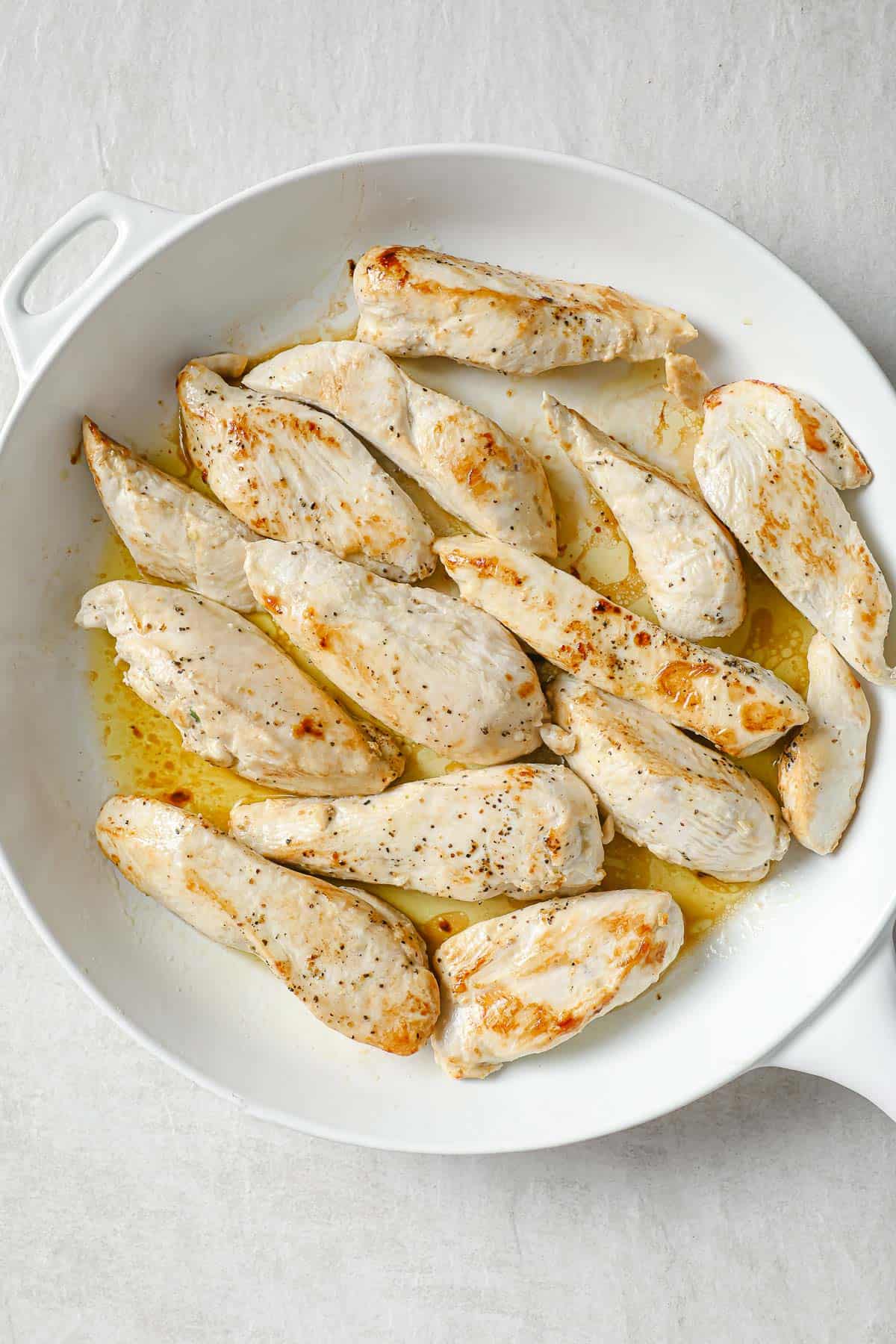 a white skilled with pan-seared chicken tenders, seasoned with salt and pepper