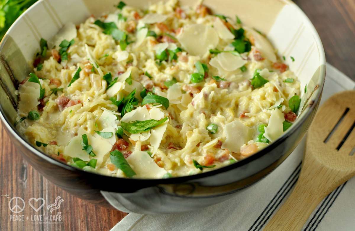 a serving bowl full of Spaghetti Squash Alfredo with Pancetta and Peas, garnished with fresh parsley and served with a wooden serving spoon