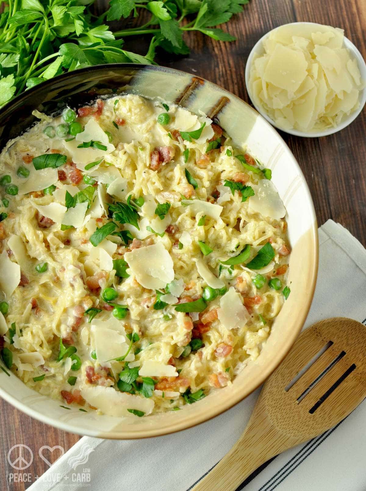 a serving bowl full of Spaghetti Squash Alfredo with Pancetta and Peas, garnished with fresh parsley and served with a wooden serving spoon