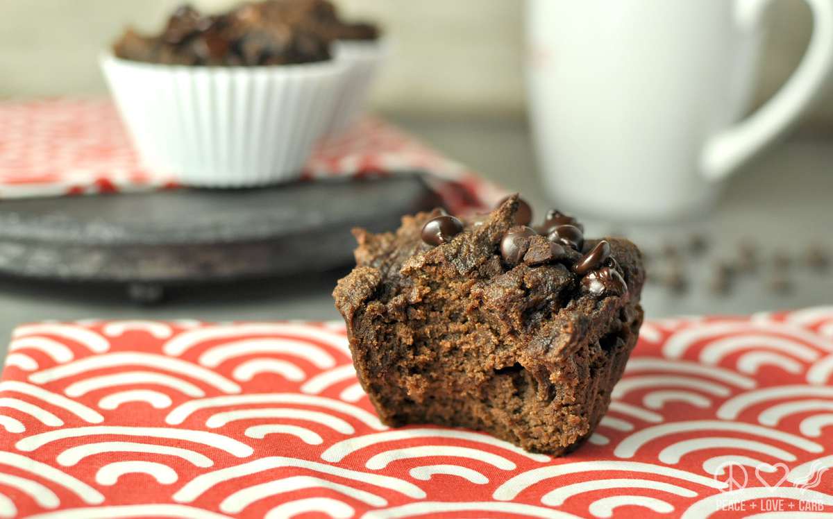 a chocolate muffin on a red and white striped towel, with more muffins and a mug of coffee in the background. 