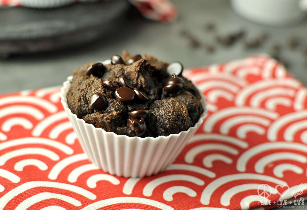 a chocolate muffin on a red and white striped towel, with more muffins and a mug of coffee in the background. 