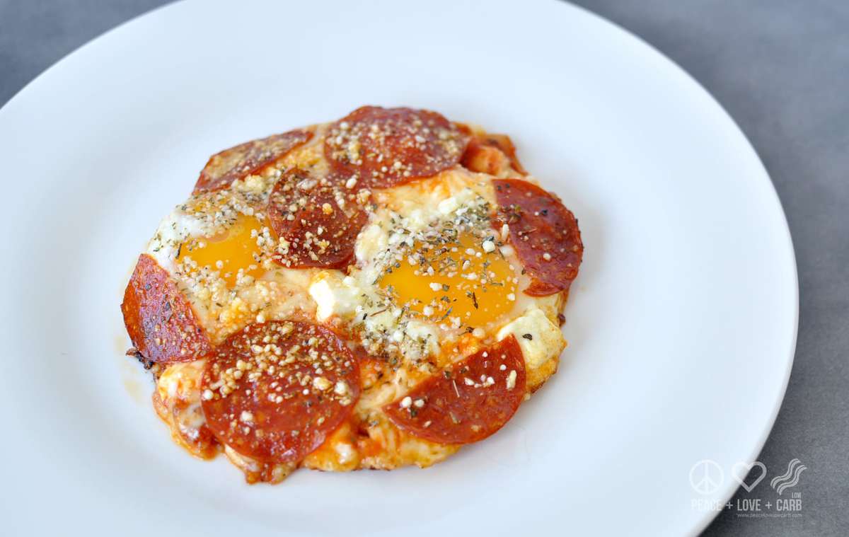 A white plate with yolky eggs, topped with pizza toppings - pepperoni, cheese, sauce, seasonings 