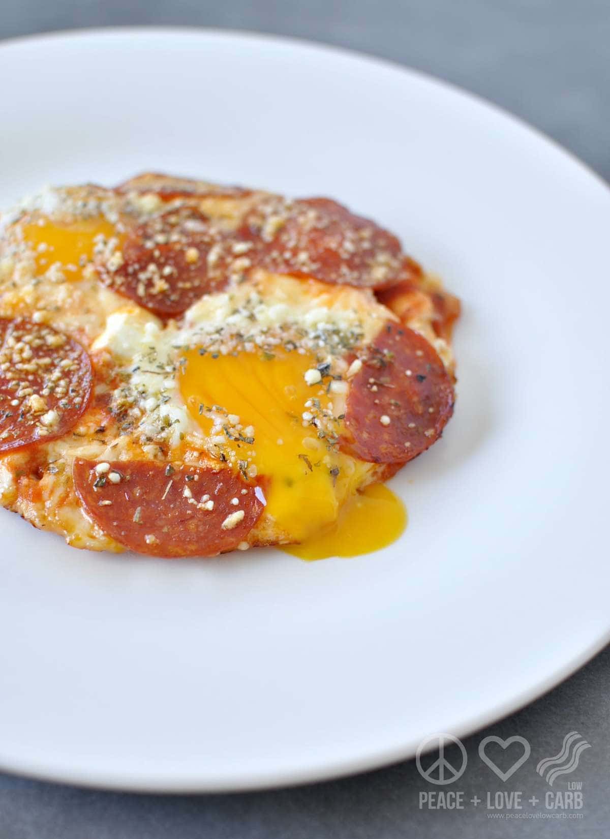 A white plate with yolky eggs, topped with pizza toppings - pepperoni, cheese, sauce, seasonings 