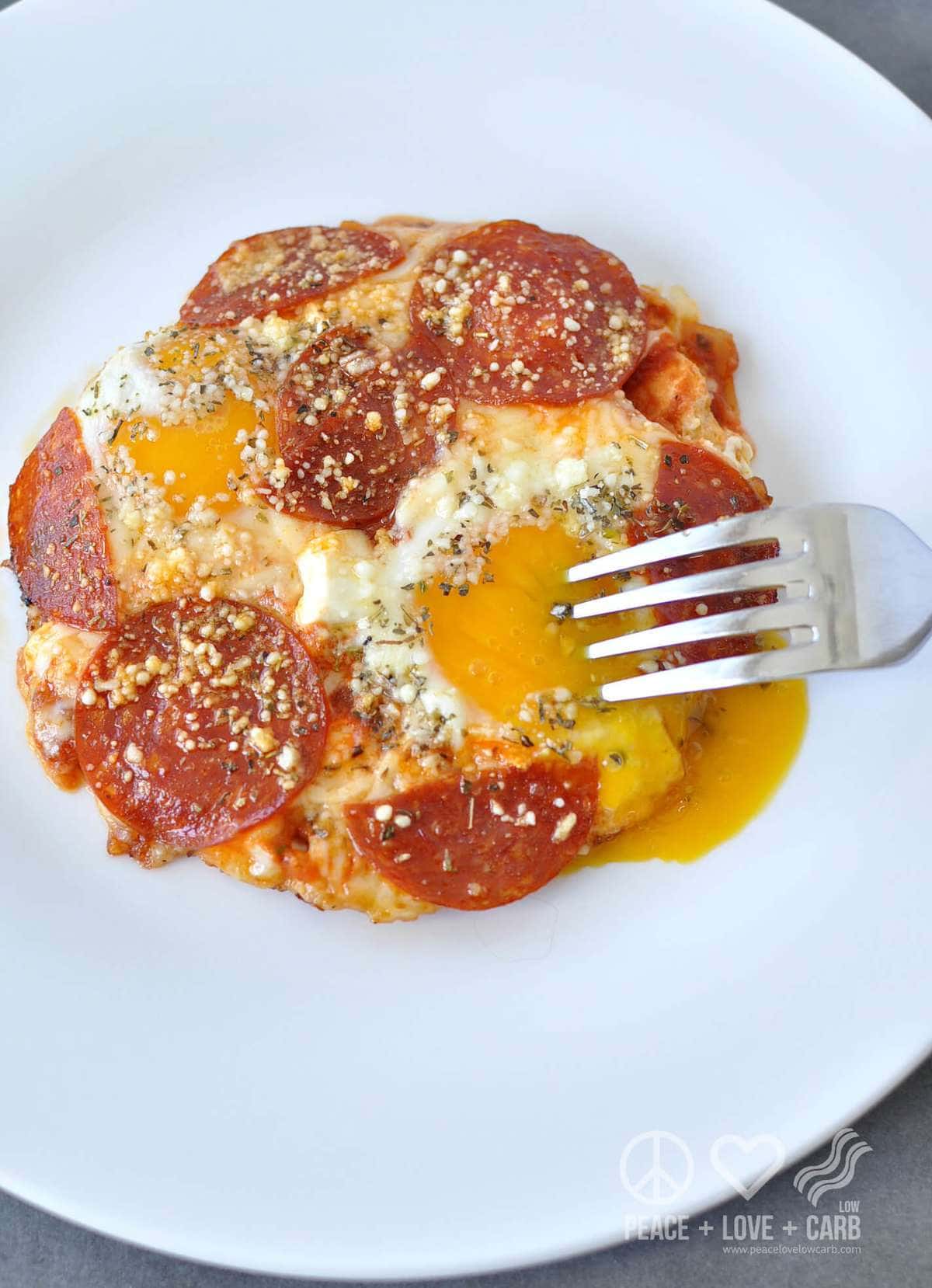 A white plate with yolky eggs, topped with pizza toppings - pepperoni, cheese, sauce, seasonings 