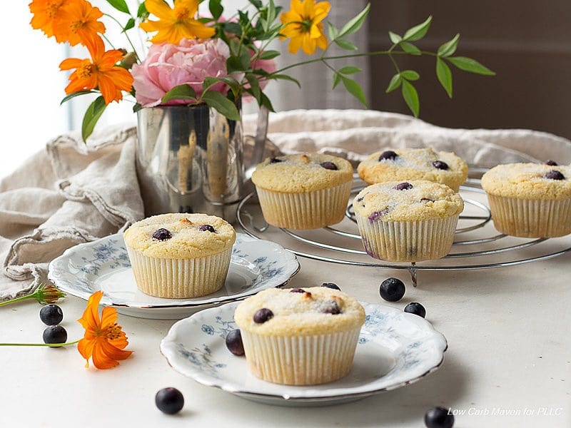 blueberry muffins on a cooling rack, with one muffin on a plate in the foreground