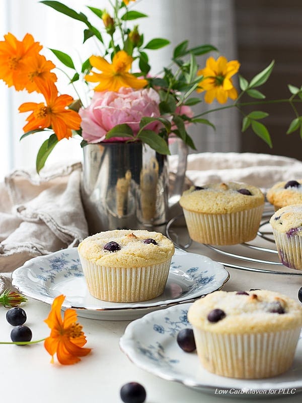 blueberry muffins on china plates, surround by fresh flowers, loose blueberries and linens