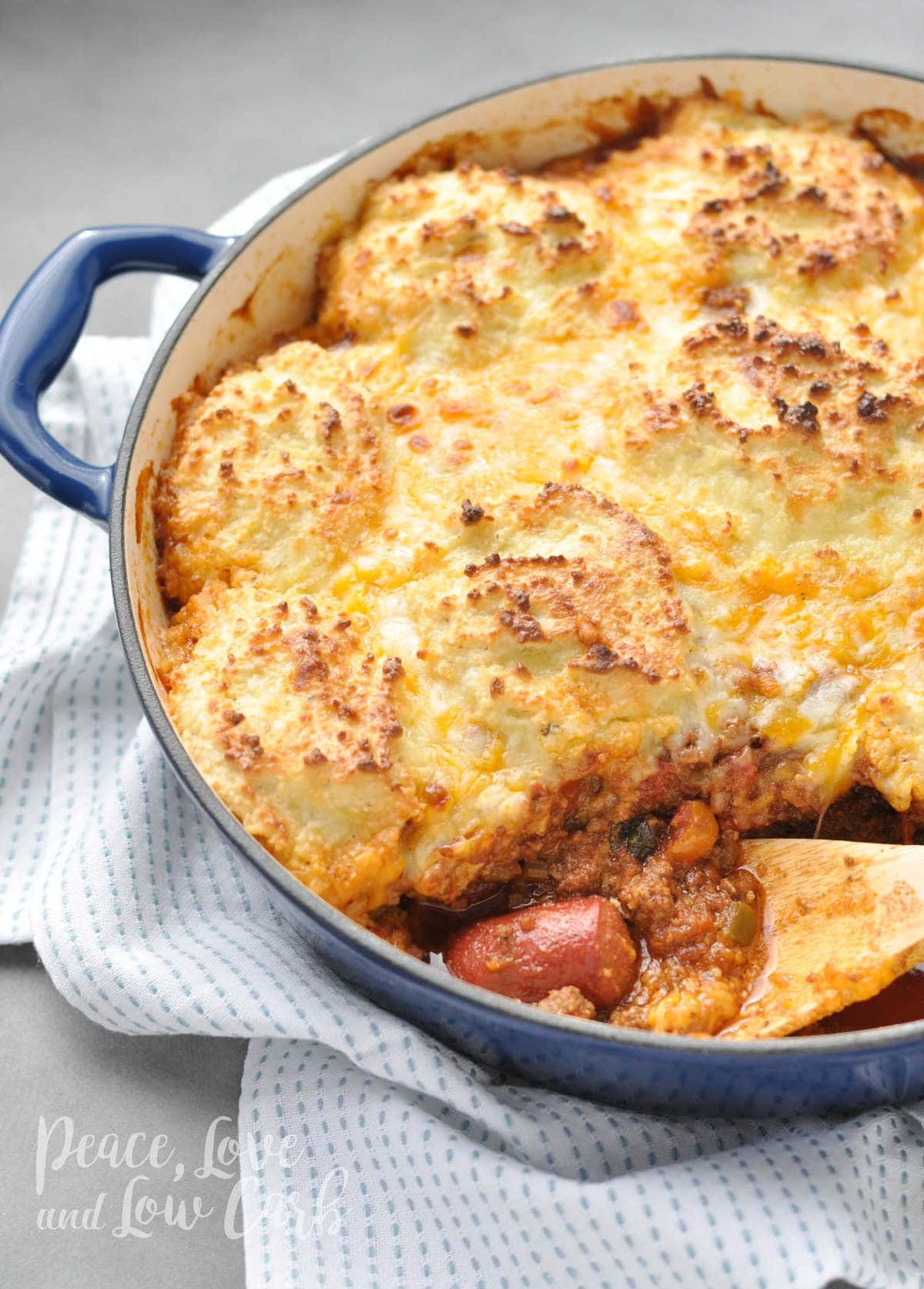 a cast iron skillet full of low carb chili, hot dogs, topped with a low carb cheesy biscuit topping