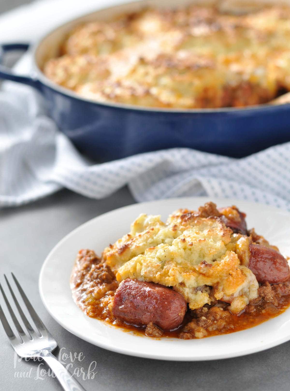 a white plate with a portion of chili dog pot pie casserole, served with a fork.