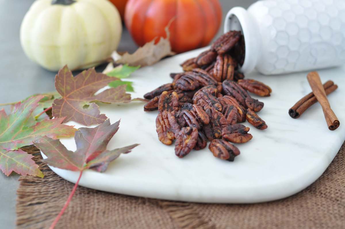 Roasted pecans, surrounded by leaves, cinnamon sticks and pumpkins.