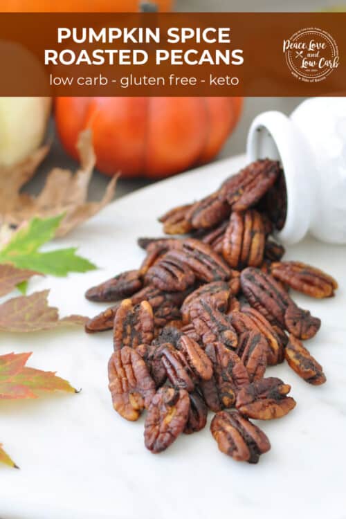 Roasted pecans spread out on a tray, surrounded by leaves, pumpkins and cinnamon sticks.