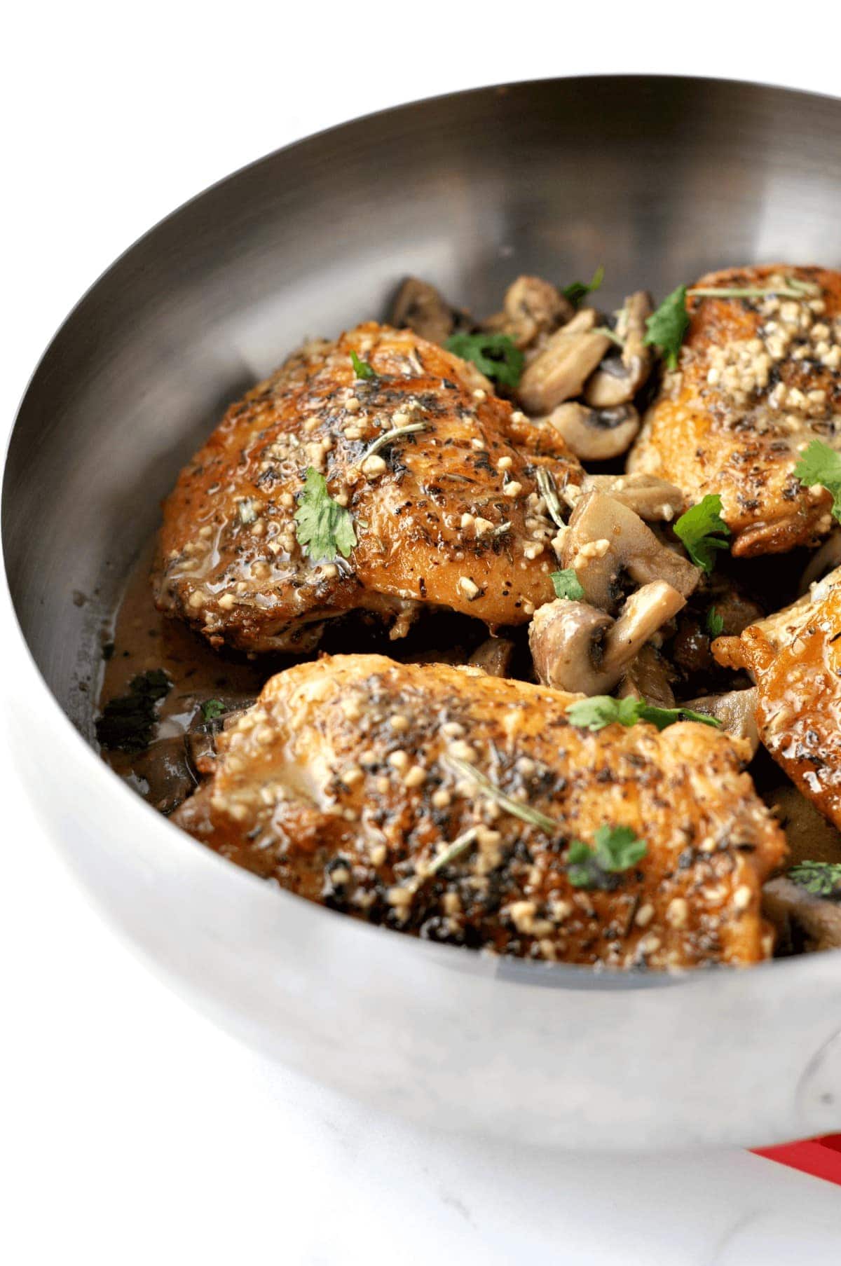 A skillet full of crispy chicken thighs, topped with a mushroom herb sauce and garnished with parsley