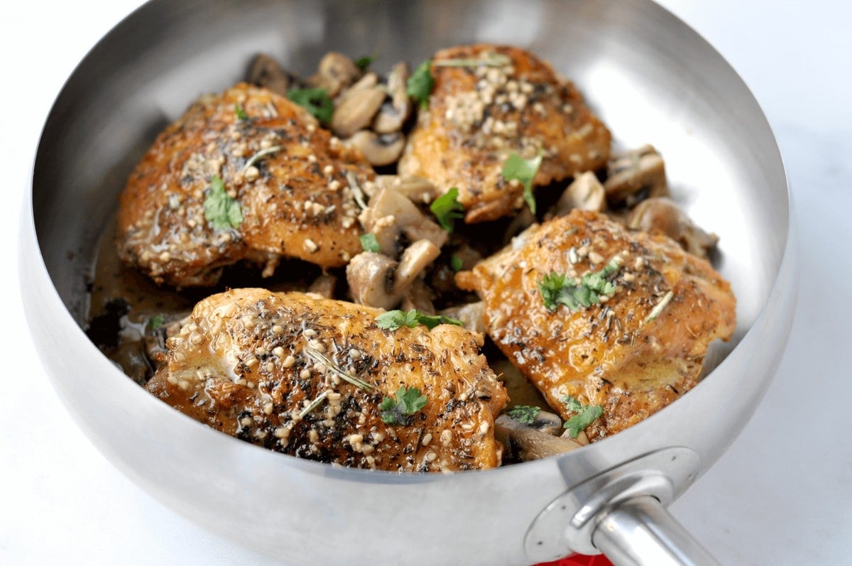 two crispy chicken thighs on a white plate, topped with a mushroom herb sauce
