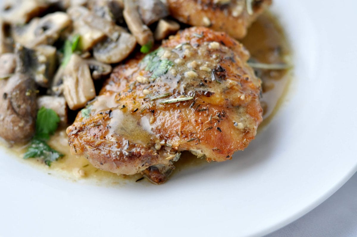 A skillet full of crispy chicken thighs, topped with a mushroom herb sauce and garnished with parsley