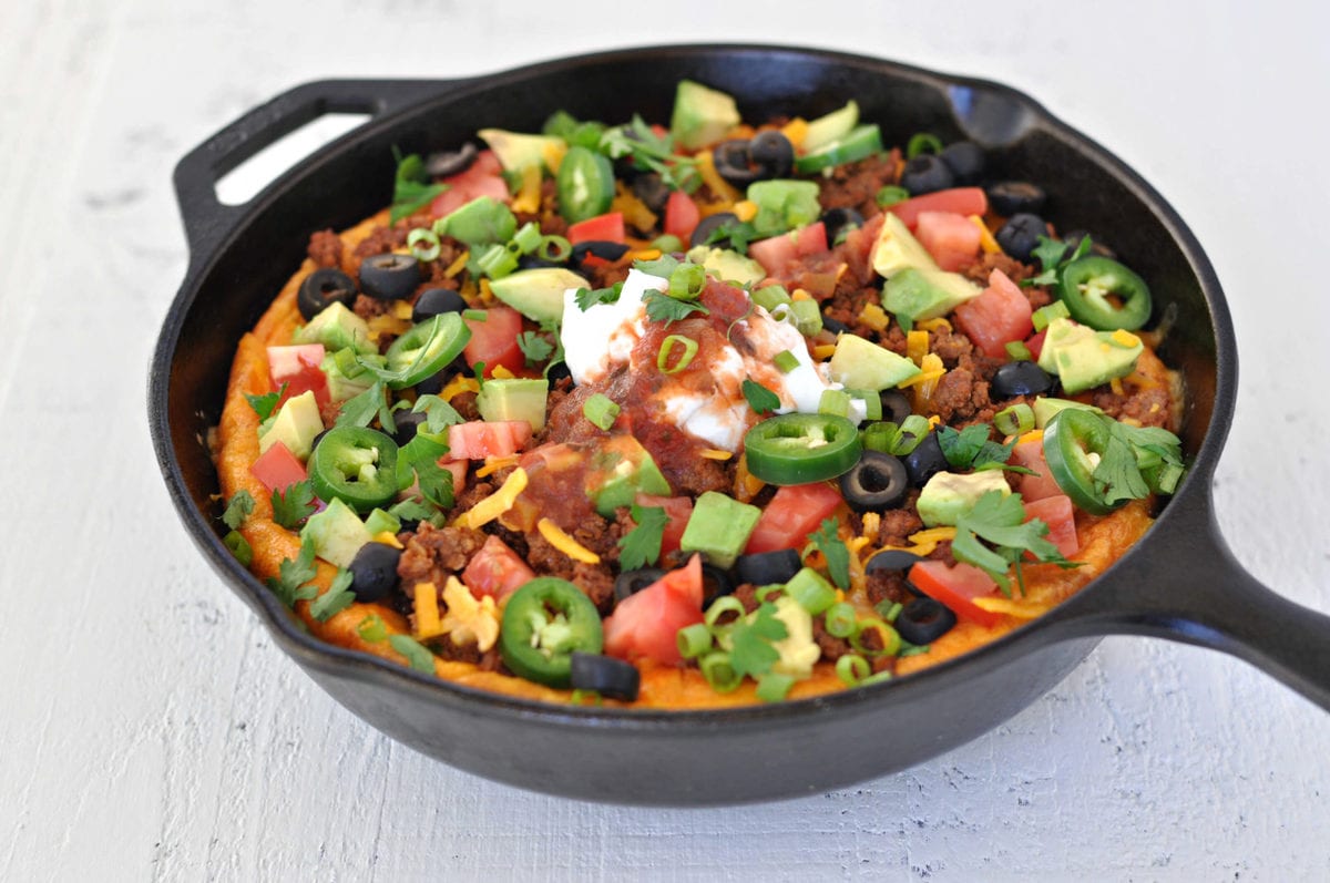 a cast iron skillet with a breakfast bake in it. Ingredients - eggs, beef, cheese, salsa, sour cream, avocado, olives.