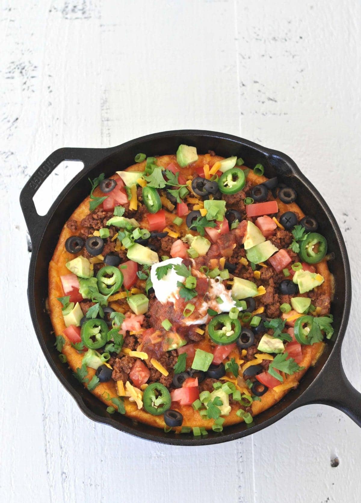 a cast iron skillet with a breakfast bake in it. Ingredients - eggs, beef, cheese, salsa, sour cream, avocado, olives.
