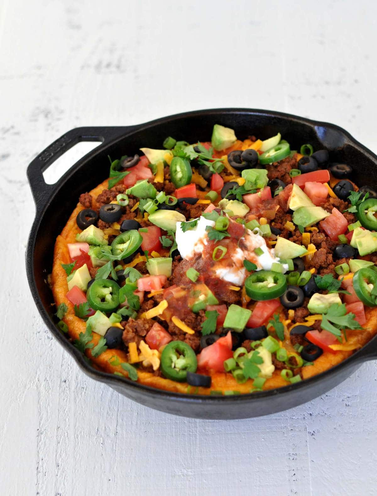 a cast iron skillet with a breakfast bake in it. Ingredients - eggs, beef, cheese, salsa, sour cream, avocado, olives.