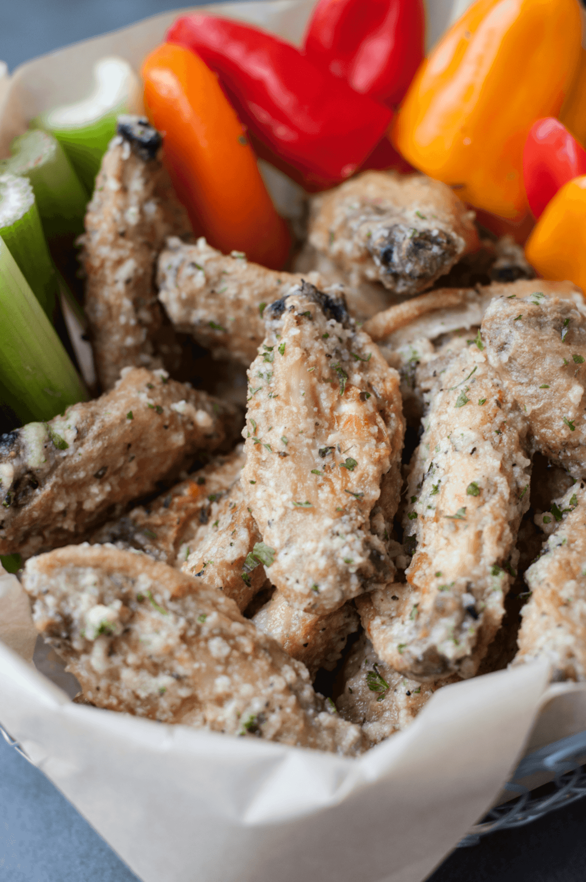 a basket lined with parchment paper, filled with chicken wings, celery, and bell peppers