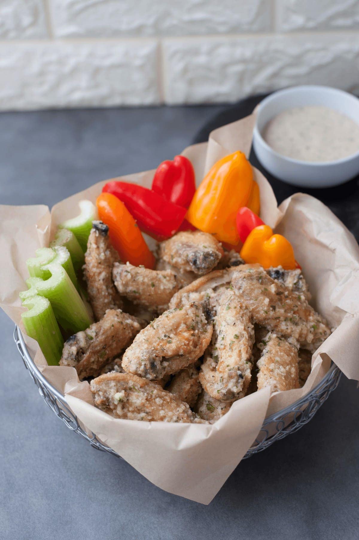 a basket lined with parchment paper, filled with chicken wings, celery, and bell peppers