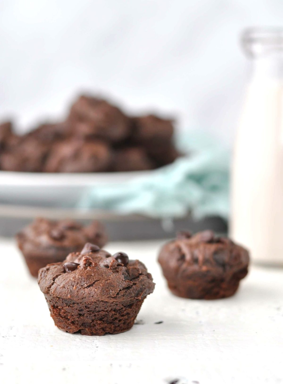 mini muffins on a white backdrop, with a basket of muffins and a jar of milk in the background.