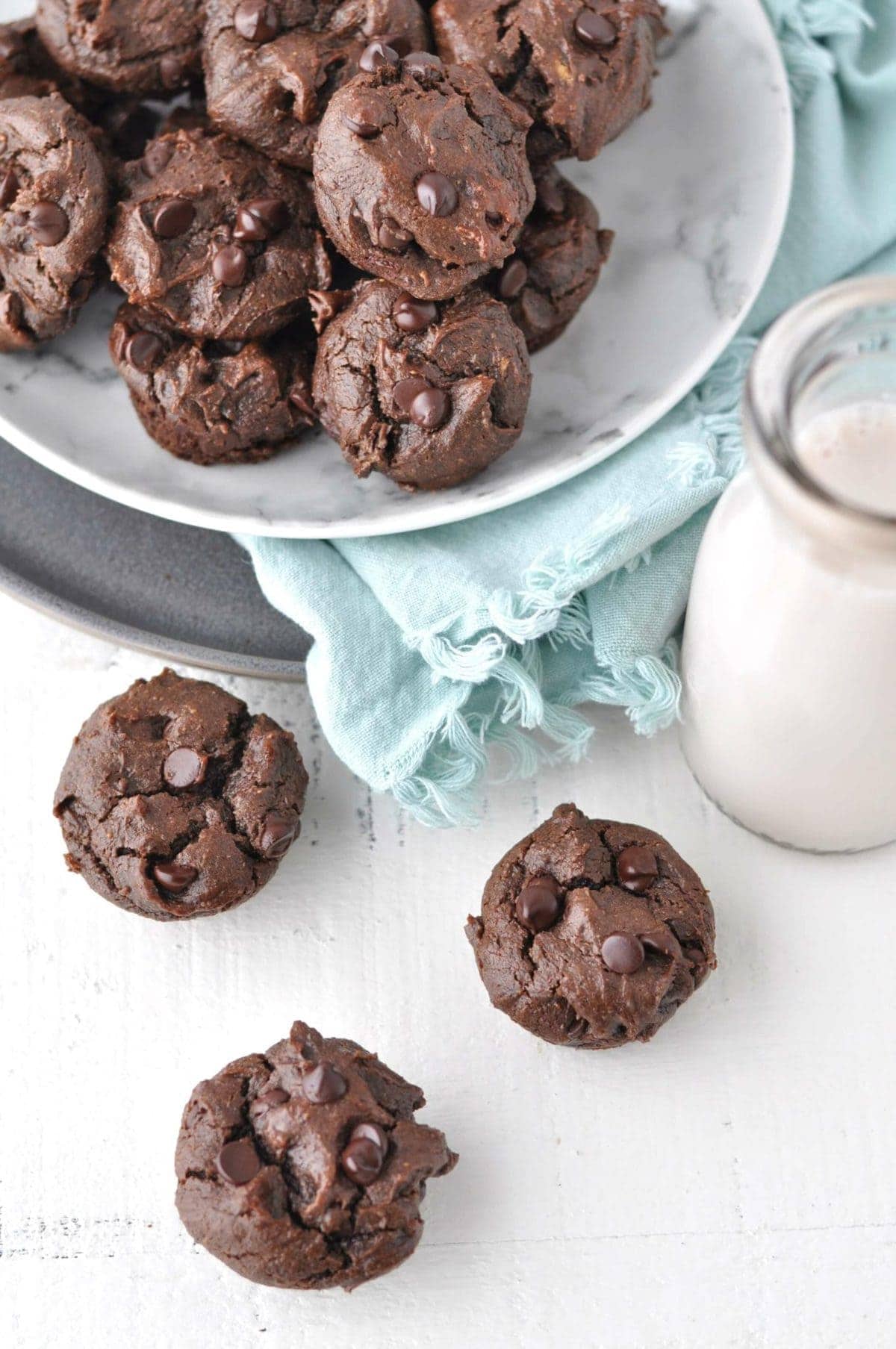 mini muffins on a white backdrop, with a basket of muffins and a jar of milk in the background.