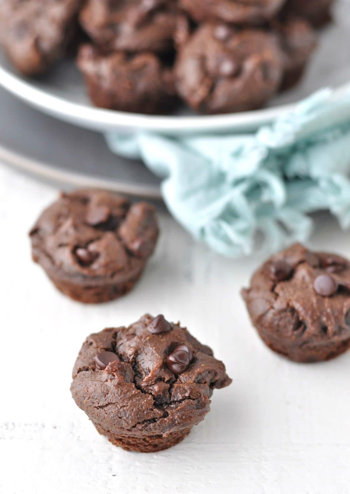 mini muffins on a white backdrop, with a basket of muffins and a jar of milk in the background.