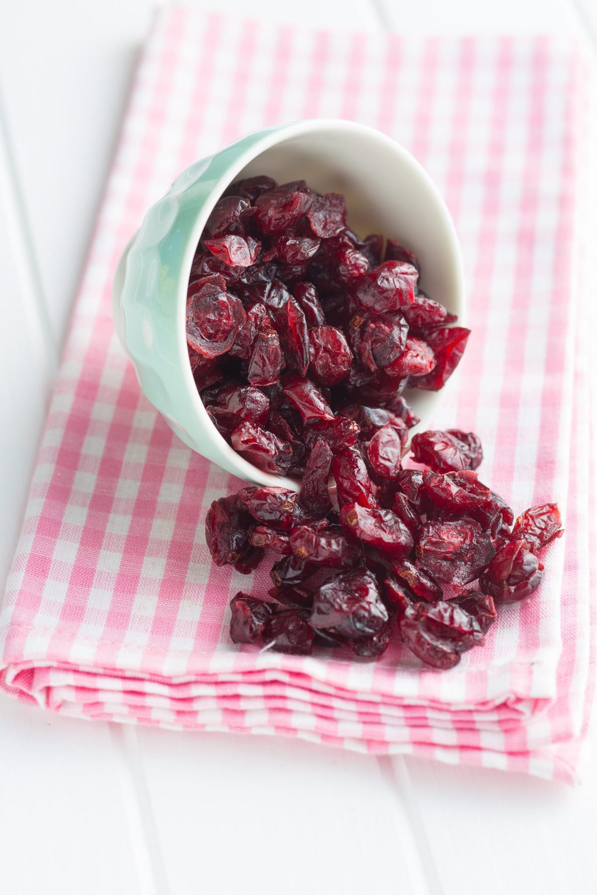 a small bowl filled with sugar free dried cranberries, tipped on its side, spilling the cranberries out onto a pink and white cloth.