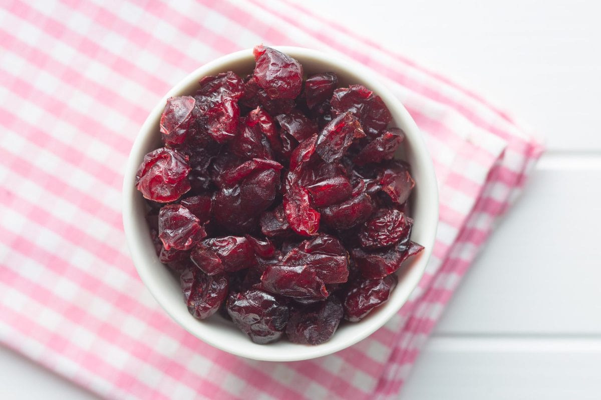 a small bowl filled with sugar free dried cranberries, tipped on its side, spilling the cranberries out onto a pink and white cloth.