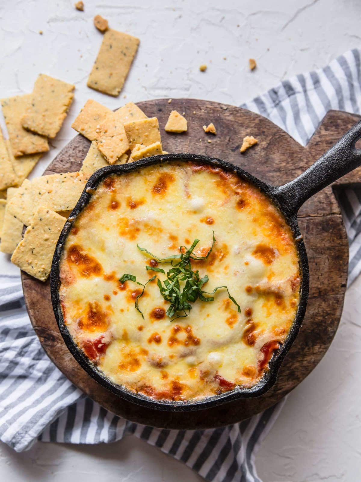 a cast iron skillet full of keto chicken parmesan dip, served with a side of low carb crackers.