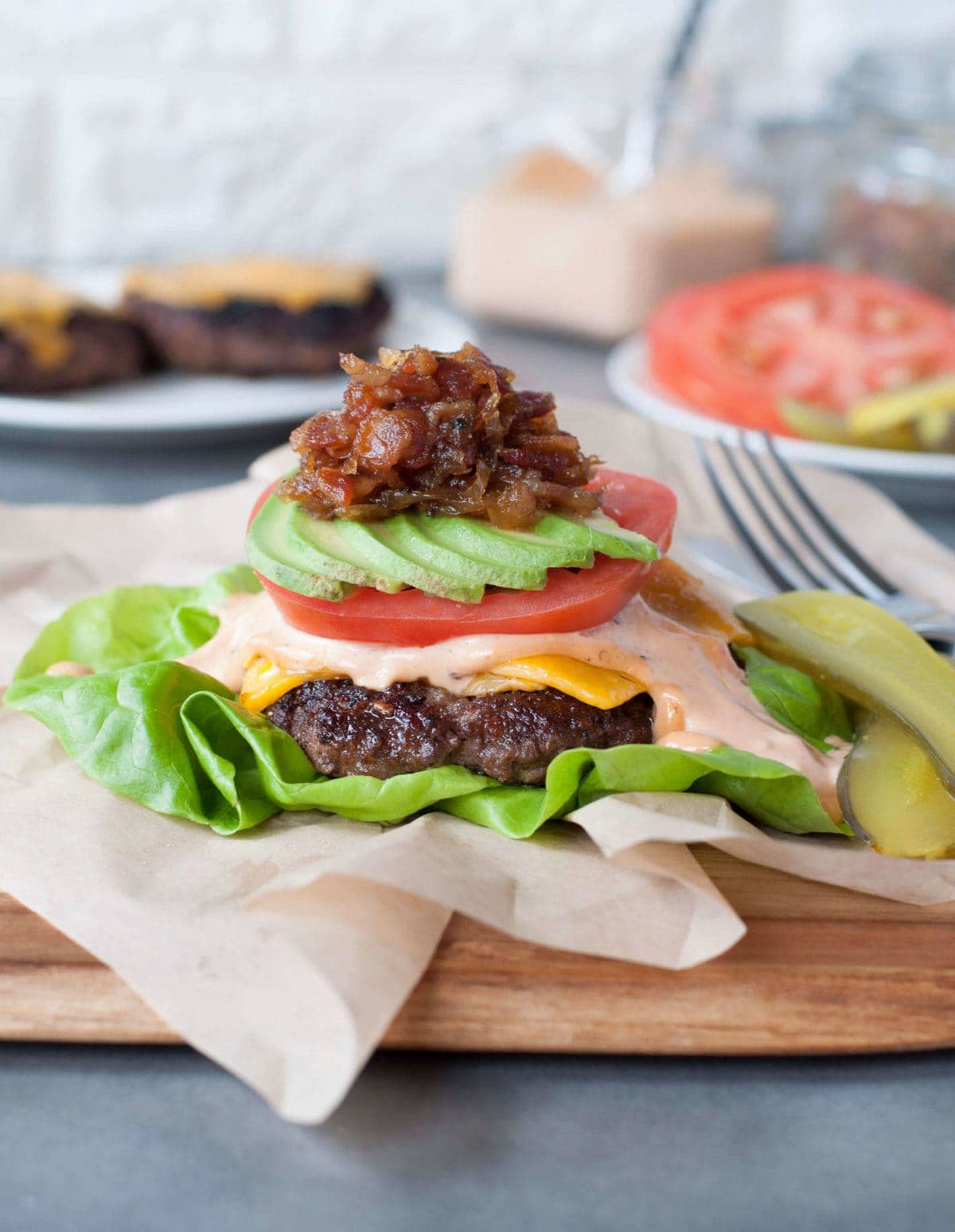 a juicy burger topped with cheese, burger sauce, tomato, avocado, bacon jam, and pickles