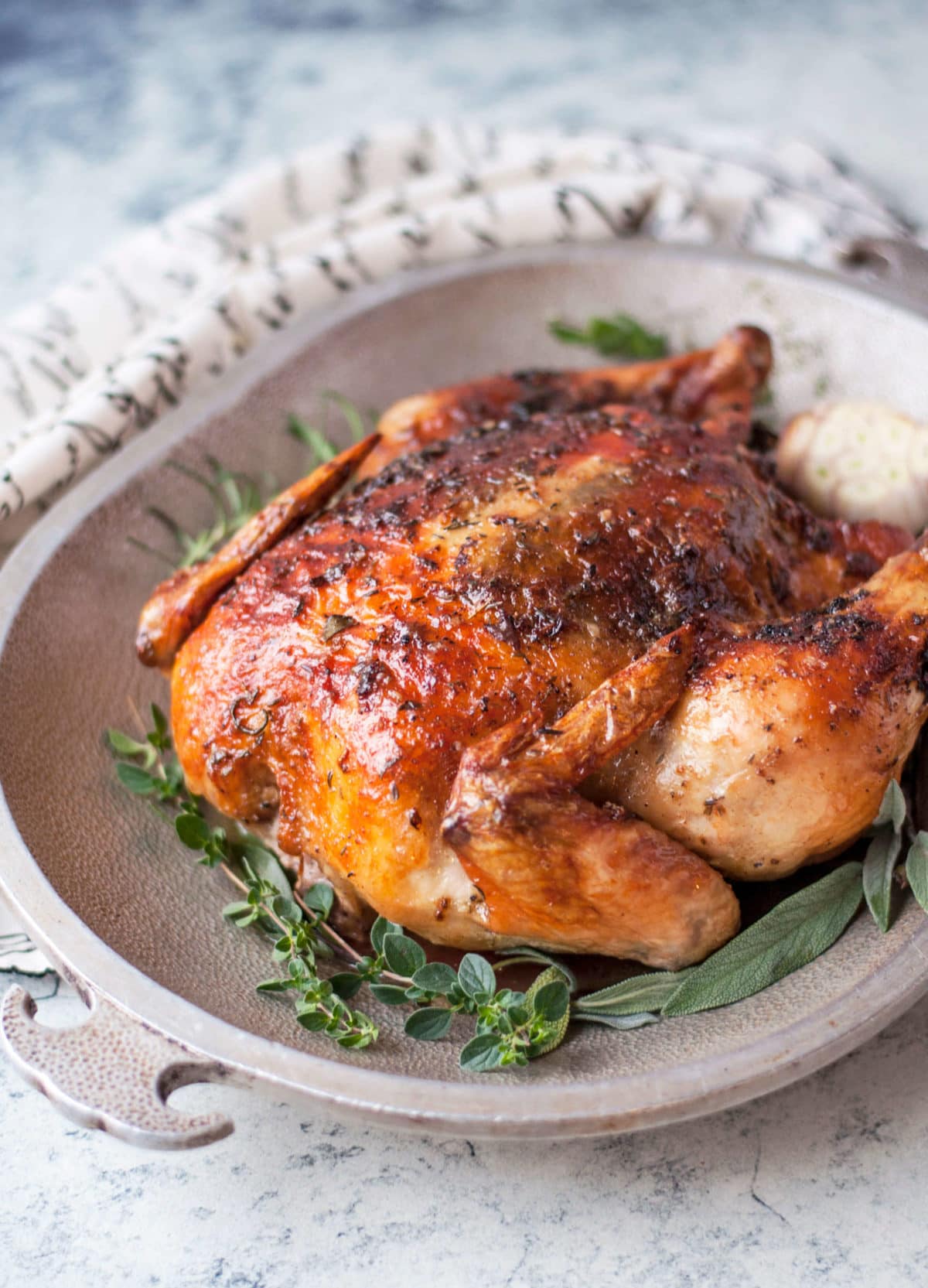 a whole roasted chicken with crispy skin on a metal platter, garnished with garlic and fresh herbs