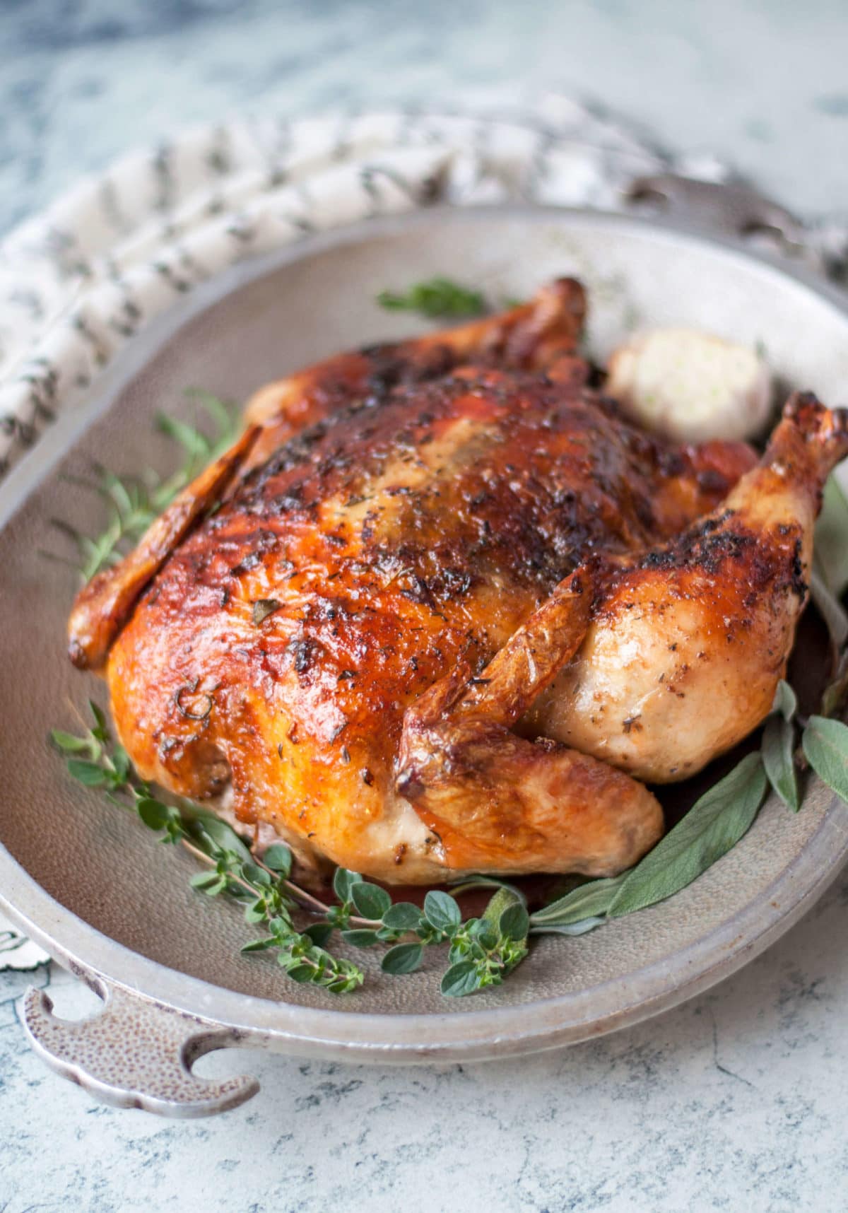 a whole roasted chicken with crispy skin on a metal platter, garnished with garlic and fresh herbs