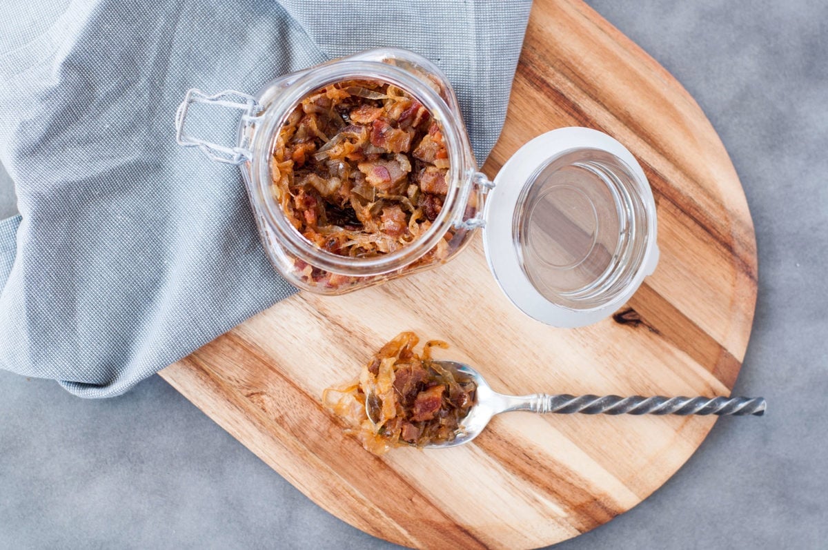 a glass jar, full of bacon jam, with a gray town and a spoon