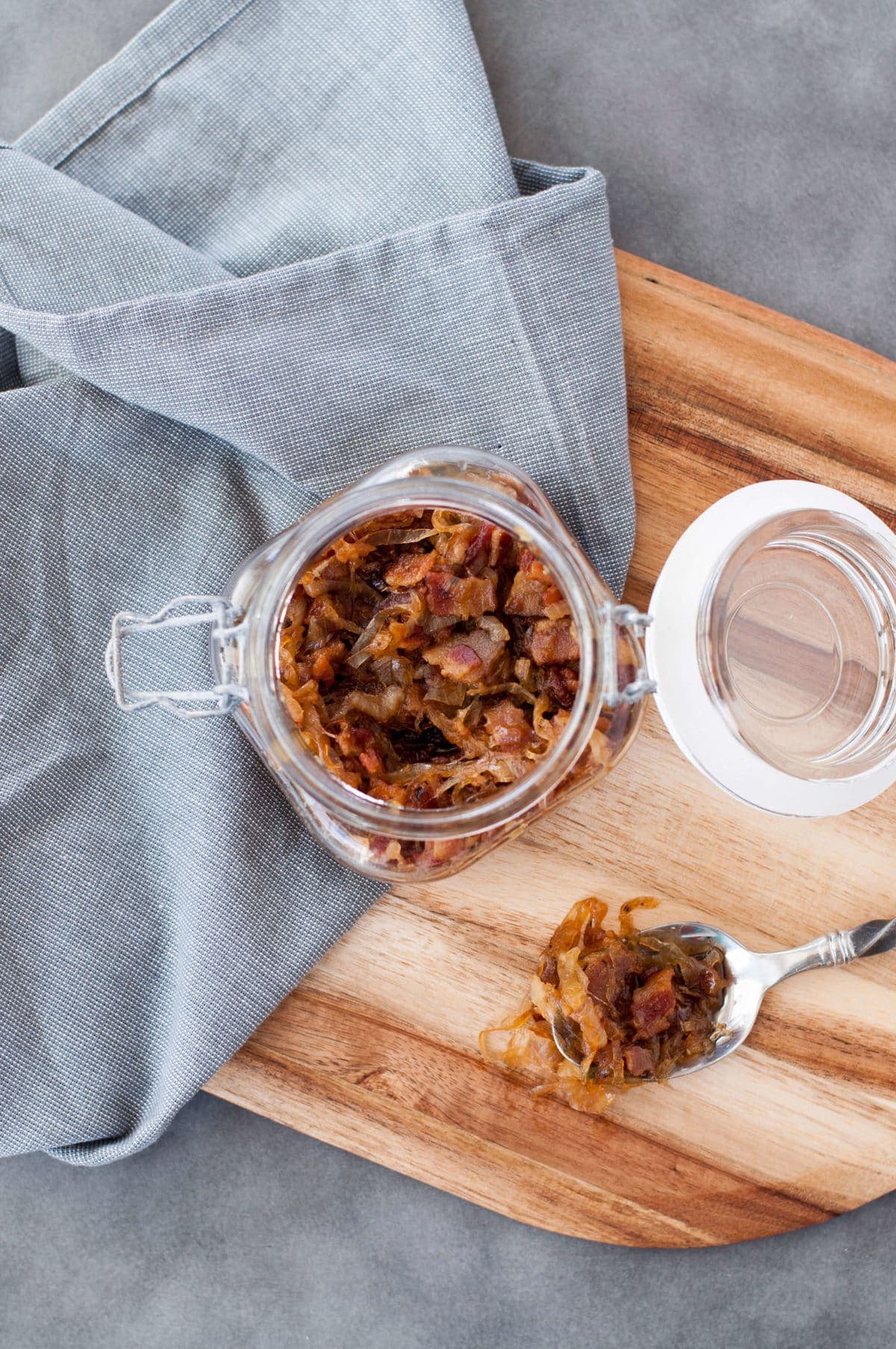 a glass jar, full of bacon jam, with a gray town and a spoon