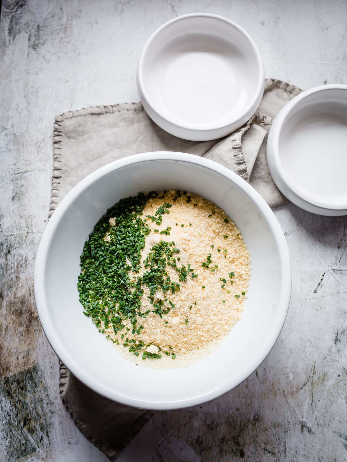 A mixing bowl with almond flour, grated parmesan cheese, garlic powder and chopped fresh chives.