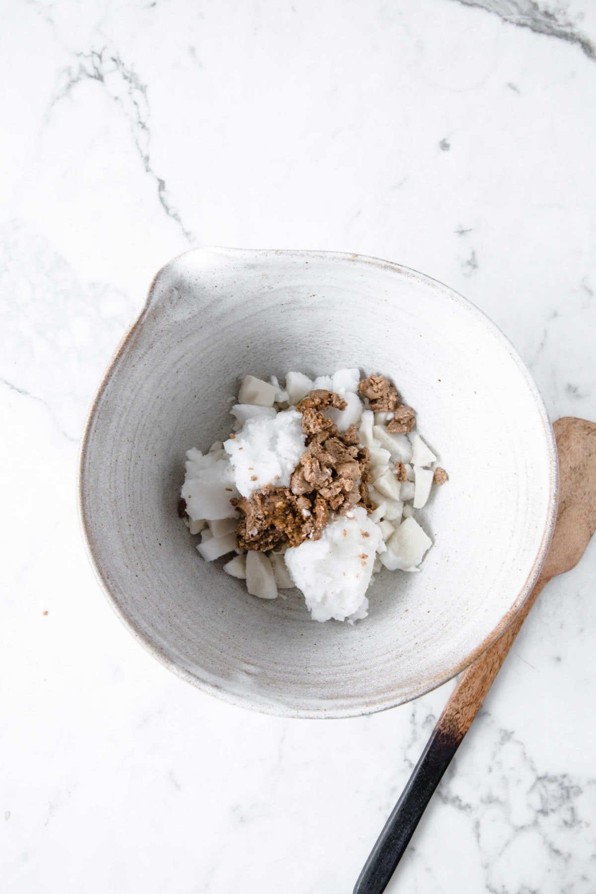 a ceramic mixing bowl with a wooden spoon with coconut oil, orange zest, and unsweetened cocoa powder