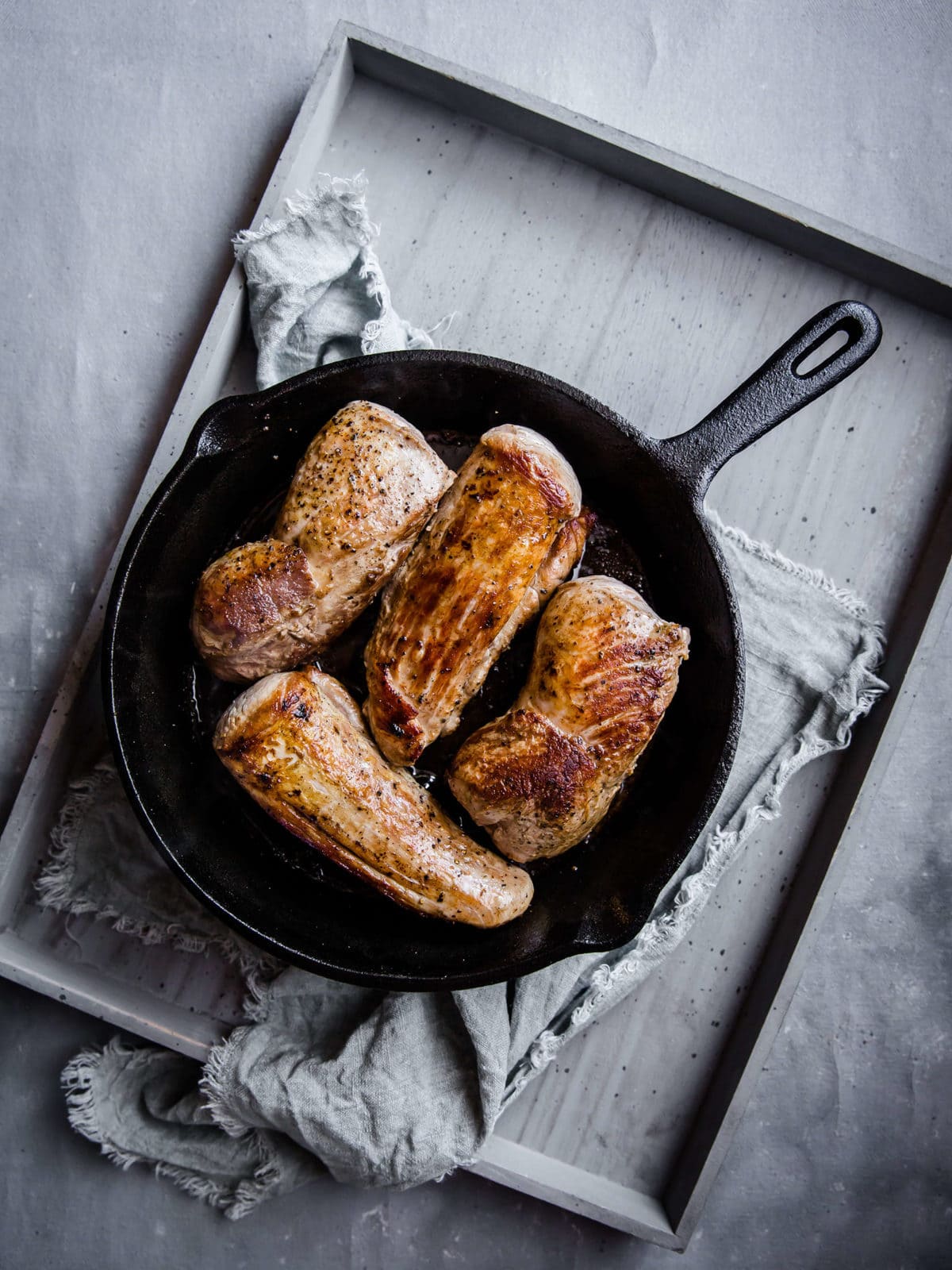 a cast iron skillet with 4 seared pork tenderloins, seasoned with a dry rub