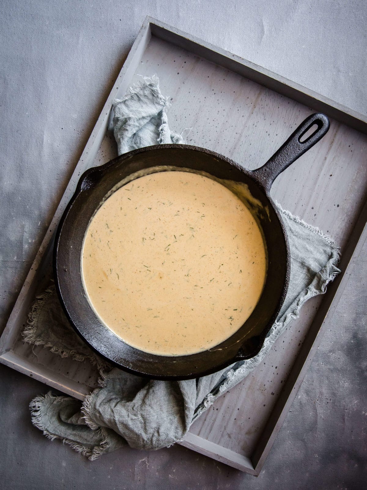 A cast iron skillet full of creamy sour cream dill sauce served on a wooden tray